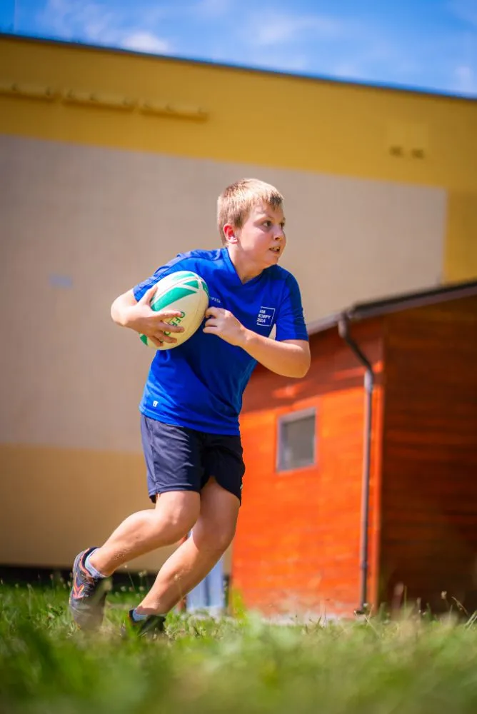 Skupina dětí v modrých tričkách drží společně trofej nad hlavami během venkovní sportovní akce.