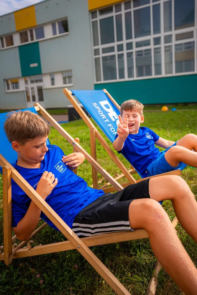 Skupina dětí v modrých tričkách drží společně trofej nad hlavami během venkovní sportovní akce.