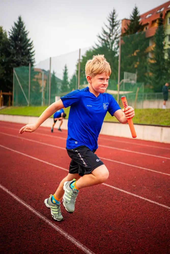Skupina dětí v modrých tričkách drží společně trofej nad hlavami během venkovní sportovní akce.