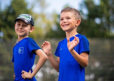 Dva chlapci v modrých tričkách stojí venku a smějí se během sportovní akce.